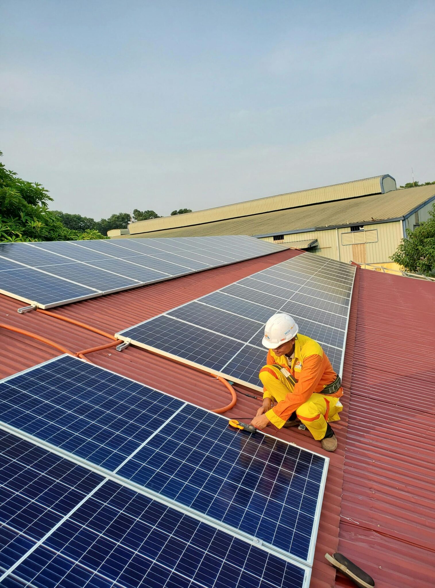 Technician working on solar panel installation on a rooftop under clear sky.