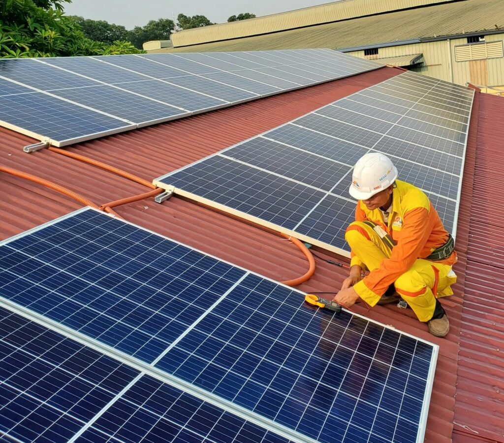 Technician working on solar panel installation on a rooftop under clear sky.