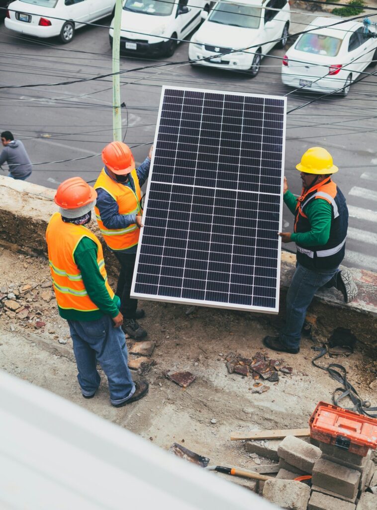 Workers in safety gear installing a solar panel outdoors.